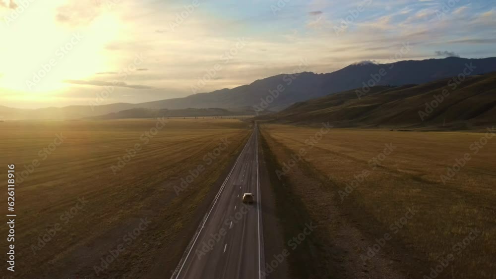 A road with yellow fields in a valley surrounded by mountains at sunset