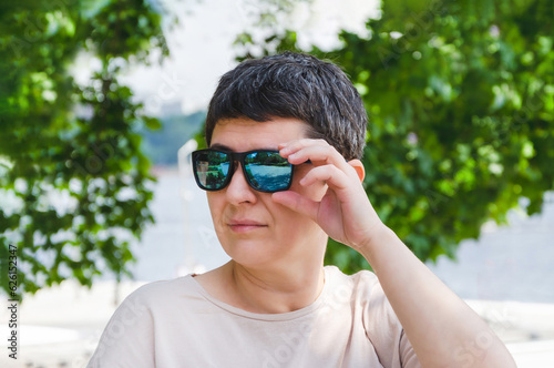 Portrait of woman with black hair and sunglasses looking into distance against backdrop of trees