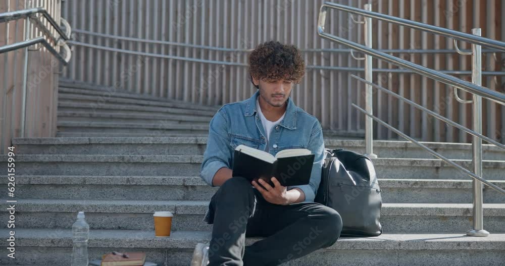 Young indian guy student reading book sitting on a stairs outdoor Young indian guy student reading book sitting on a stairs outdoor