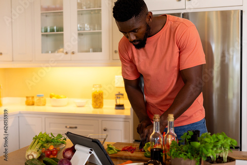 African american man chopping vegetables using tablet in kitchen