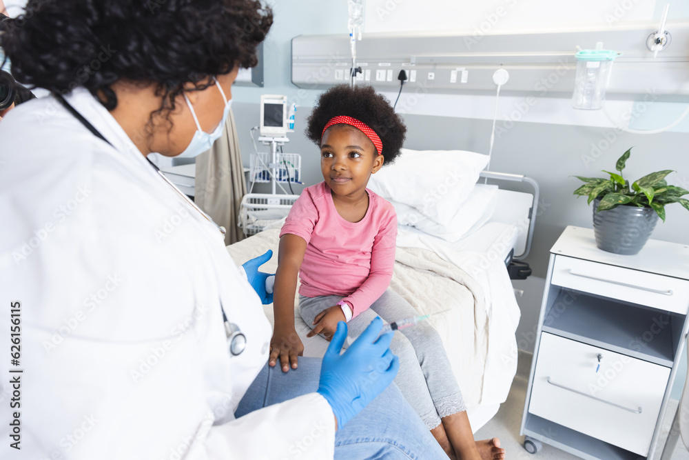 Fototapeta premium African american female doctor wearing face mask vaccinating girl patient at hospital