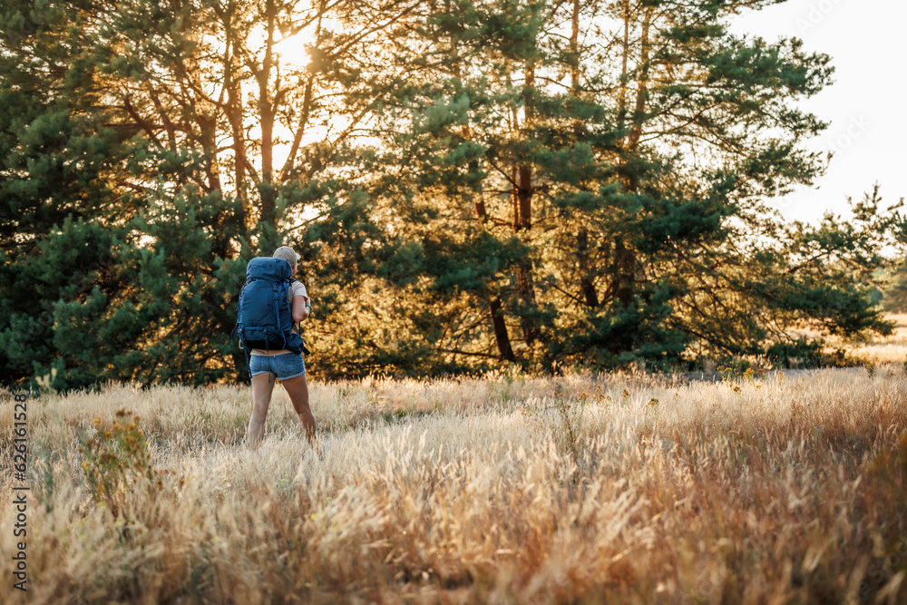 Woman with backpack hiking in forest during sunset. Trekking in wilderness alone. Summer adventure in nature