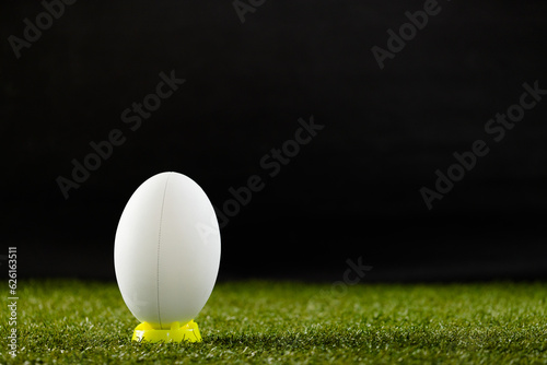 White rugby ball in yellow stand over grass with copy space, in slow motion