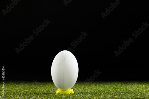White rugby ball in yellow stand over grass with copy space, in slow motion