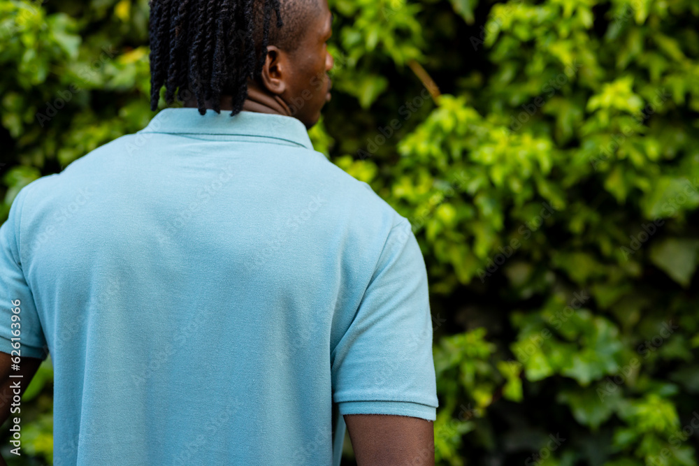 Rear view of african american man with dreadlocks wearing pale blue polo shirt in garden, copy space Rear view of african american man with dreadlocks wearing pale blue polo shirt in garden, copy space
