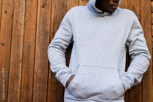 Canvas Print Midsection of african american man wearing grey hooded sweatshirt against wooden
