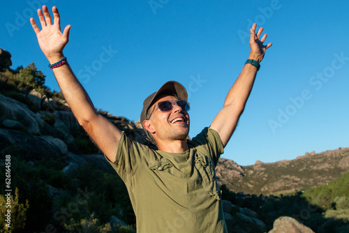 Man dressed in military green t-shirt and cap and sunglasses enjoying a day in the mountains