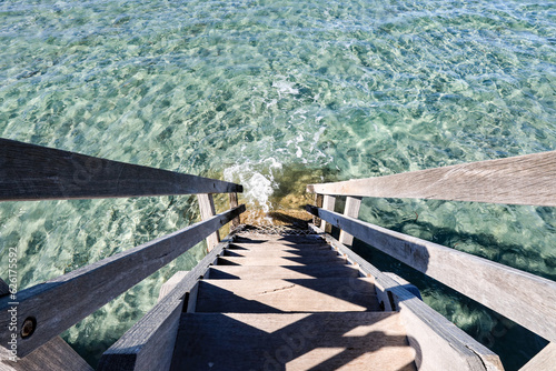 View looking down timber stairs of jetty into clear ocean water photo