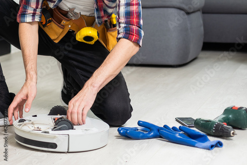 Robot vacuum cleaner repair. Man fixing robot vacuum cleaner DIY at home on the floor. Robotic vacuum cleaner maintenance and service. Smart device for easy housework. New tech for households.