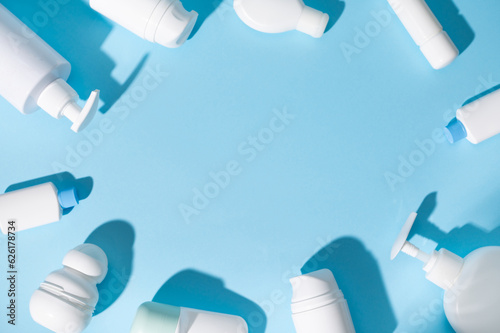 Flat lay of white bottles with body lotion, moisturizer, facial anti-aging serum laid out on isolated blue background
