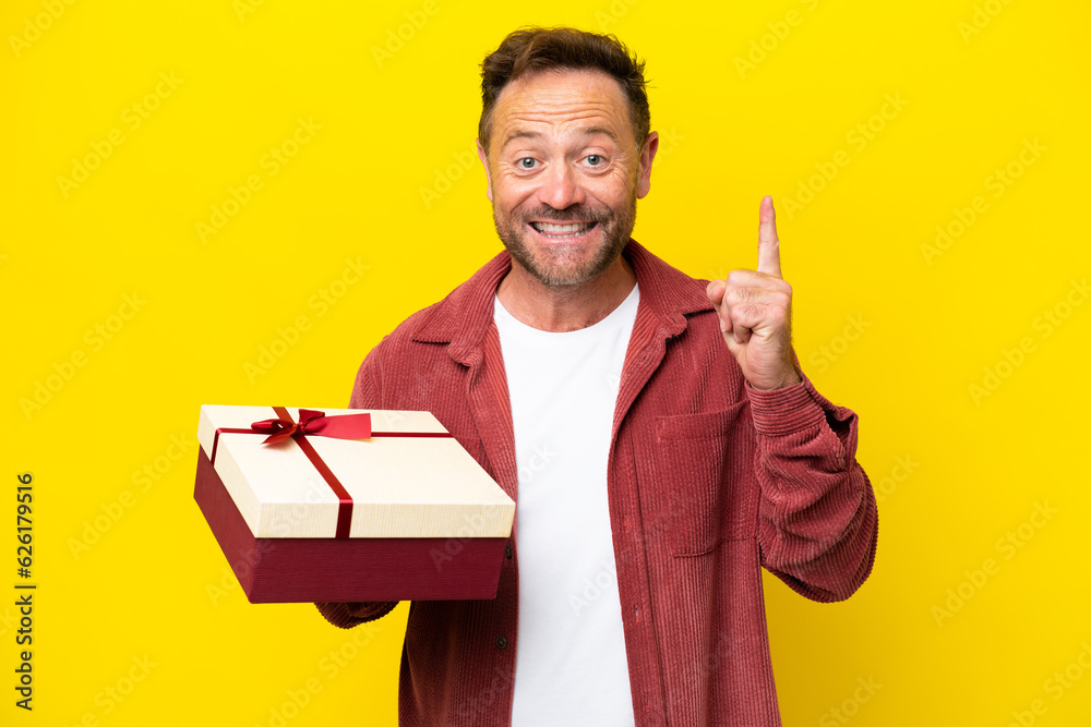 Middle age caucasian man holding a gift isolated on yellow background pointing up a great idea Middle age caucasian man holding a gift isolated on yellow background pointing up a great idea