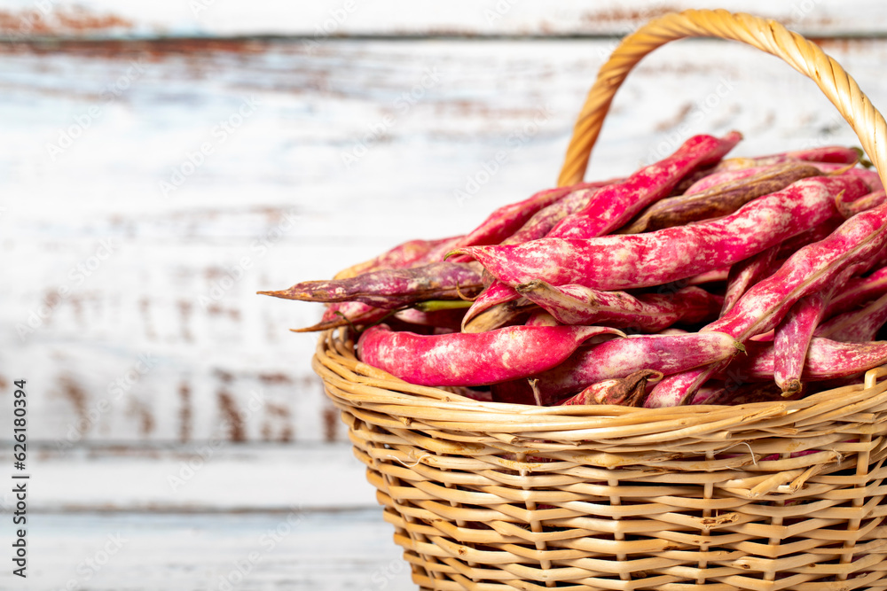 Fresh kidney beans in a wicker basket over wooden background. Pinto beans or cranberry beans harvest season concept. Vegetables for a healthy diet. Copy space. Empty space for text