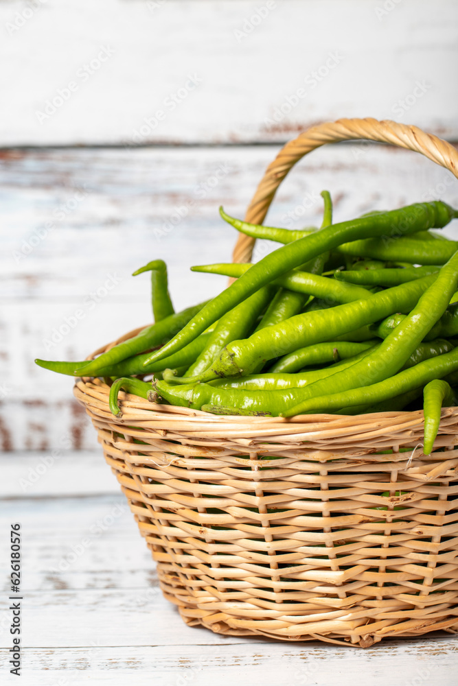 Fresh green pepper in a wicker basket over wooden background. Green chili pepper harvest season concept. Vegetables for a healthy diet. Close up Fresh green pepper in a wicker basket over wooden background. Green chili pepper harvest season concept. Vegetables for a healthy diet. Close up