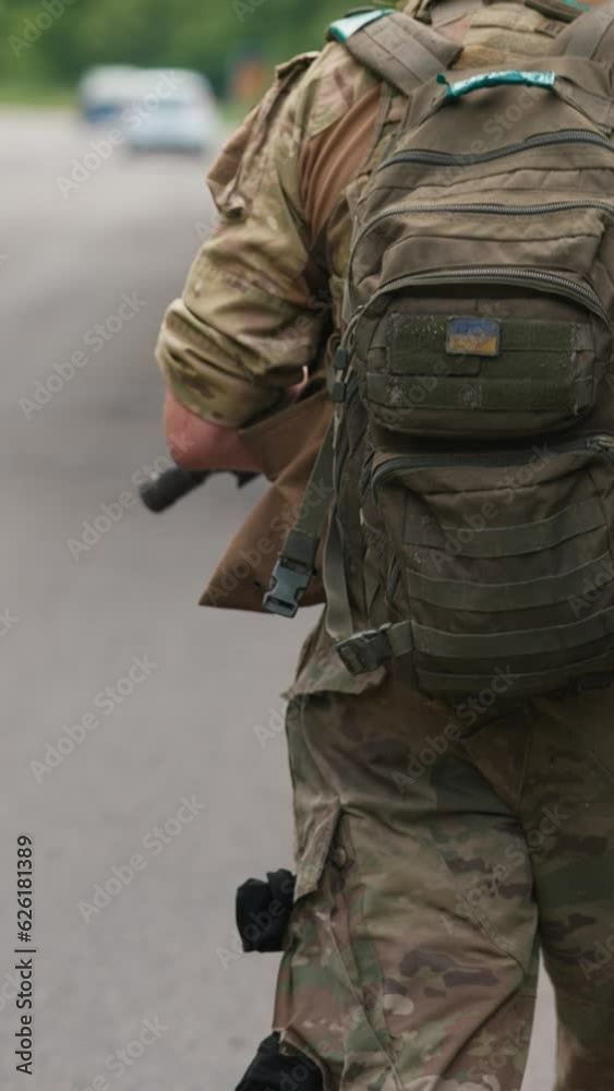 Armed forces member with a firearm and a backpack is advancing along the road. Armed forces member with a firearm and a backpack is advancing along the road.