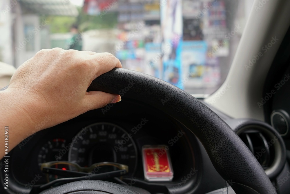 A hand on the steering wheel of a car with blurred background, travel concept.