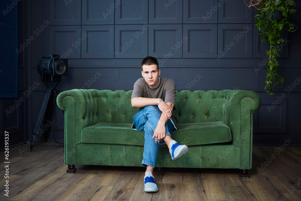A handsome young boy is sitting on the sofa in the studio. Stylish loft-style interior. A handsome young boy is sitting on the sofa in the studio. Stylish loft-style interior.