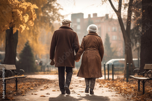 Enduring love and devotion of an old couple as they hold hands and walk together through a picturesque autumn park, celebrating a lifetime of affection and cherished memories. Ai generated