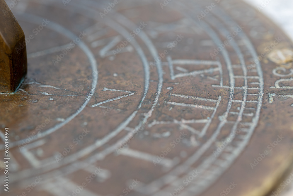 Close up detail of an old metal sun dial with roman numerals and compass point directions. Narrow depth of field to create a more abstract image.
