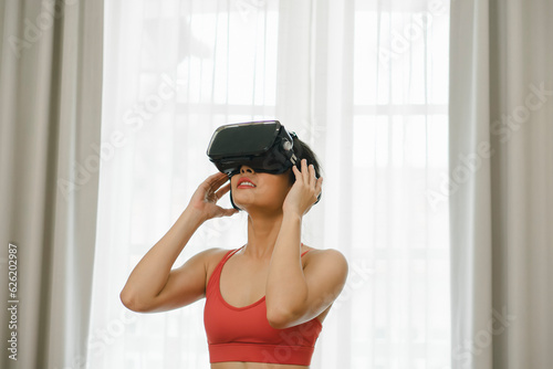 Immersed in her fitness routine, an Asian woman engages in a virtual reality workout at home, fully experiencing the benefits of virtual exercise.