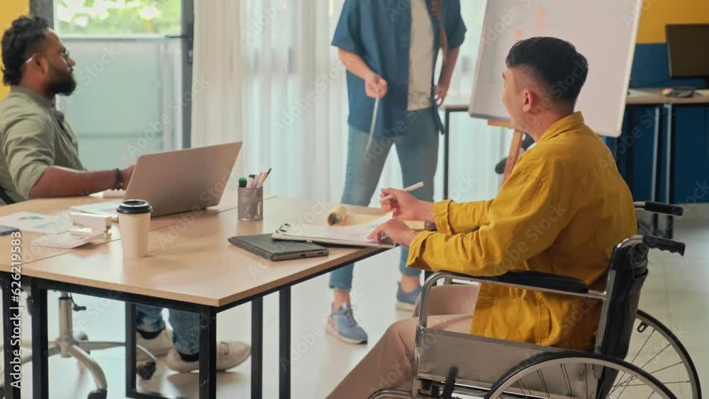 Medium shot of man in wheelchair having meeting with co-workers discussing work projects at office Medium shot of man in wheelchair having meeting with co-workers discussing work projects at office