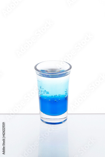 Blue cocktail in a shot glass on a mirror counter bar isolated on white background.