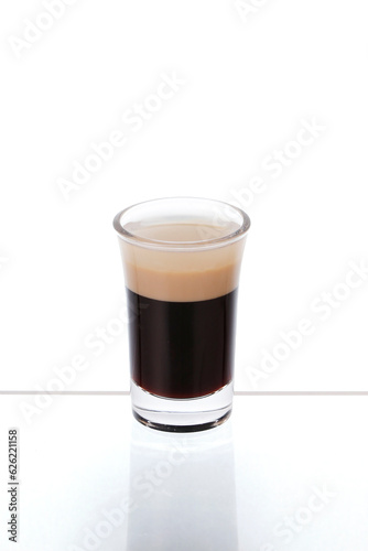 B-52 Cocktail in a shot glass on a mirror counter bar isolated on white background. Separation layer between Coffee liqueur, Irish cream Liqueur and Orange Cognac.