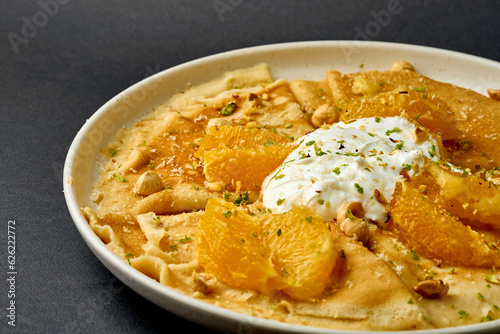 Crepes suzette with ice cream, nuts and oranges on a dark background.