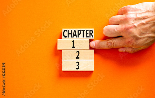 Time to chapter 1 symbol. Concept word Chapter 1 2 3 on wooden block. Businessman hand. Beautiful orange table orange background. Business planning and time to chapter 1 concept. Copy space.