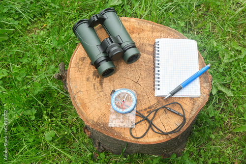 military binoculars, notebook and compass in nature on a stump