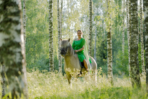 Barefoot woman rider on Icelandic horse in sunny Finnish brirch forest during sunset. Fairytale like feeling.