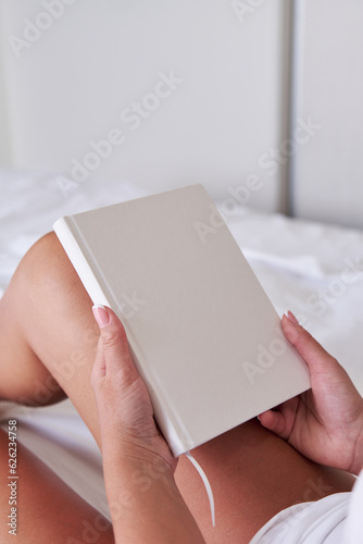 Wallpaper Mural Young woman holding blank notebook or book mockup with white cover while sitting on the bed. Torontodigital.ca