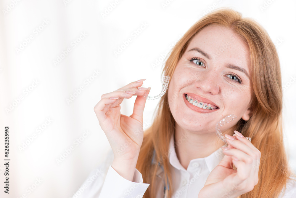 Dental care.Smiling girl with red hair holding heart shaped aligners Dental care.Smiling girl with red hair holding heart shaped aligners