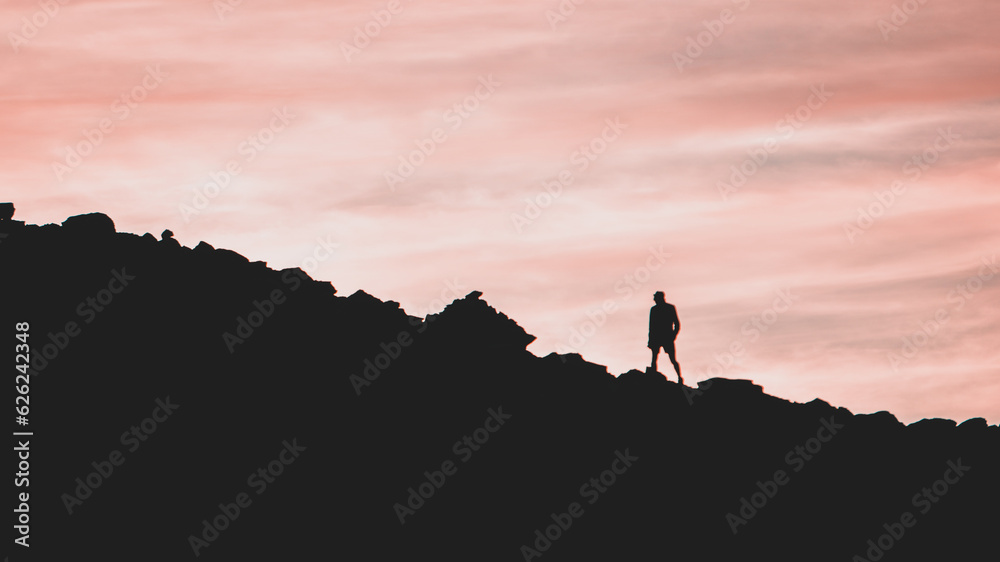 Silhouette of one person walking on the edge of the hill at sunset Silhouette of one person walking on the edge of the hill at sunset