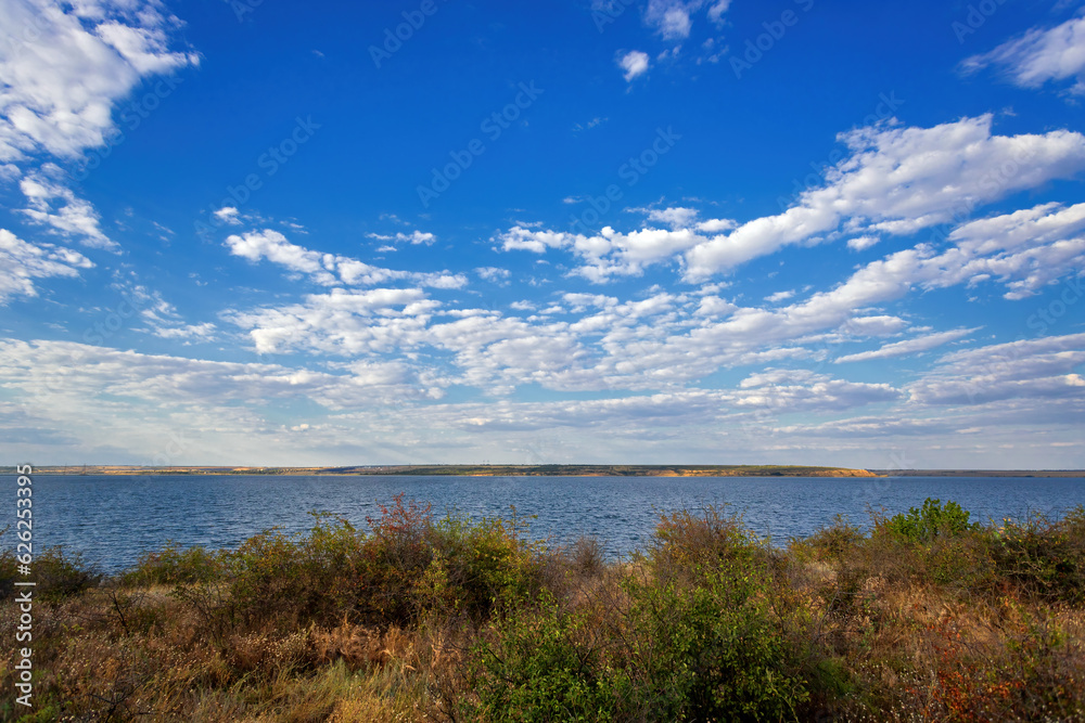 Summer lakeside, blue sky with white clouds, soft evening light