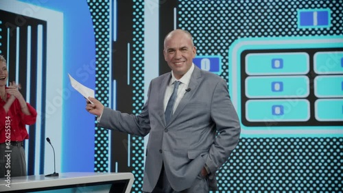 Funny charismatic host talking to the camera during recording of a fictional morning family game show