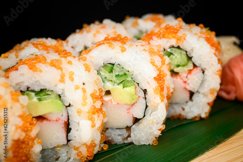 Closeup view of freshly made tasty california rolls covered with orange tobiko caviar served on banana leaves on black background