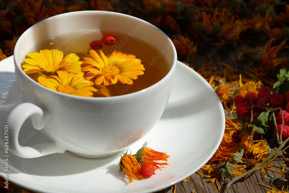 Tea with fresh calendula flowers in a white cup. There are also dried calendula flowers on the table. Tea with fresh calendula flowers in a white cup. There are also dried calendula flowers on the table.