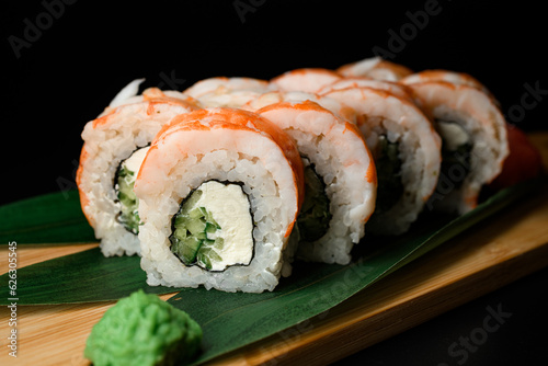 Sushi pieces with shrimp served on wooden board with plant leaves and wasabi