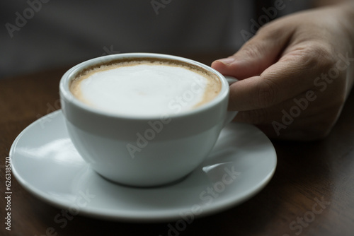 Closeup hand holding white cup of hot coffee latte on wood background in restaurant.Best of menu in the coffee shop.Soft focus.