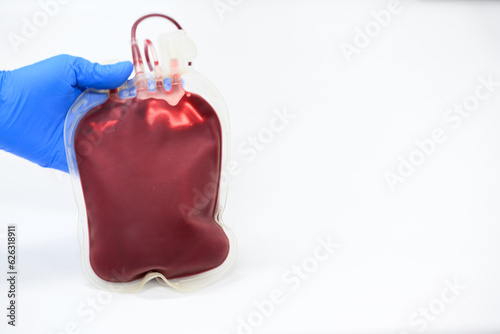 Doctor hand wearing blue glove holding blood pack for transfusion from donor.Full blood bag for accident's patient on white background in blood bank unit at laboratory.Safe life concept.