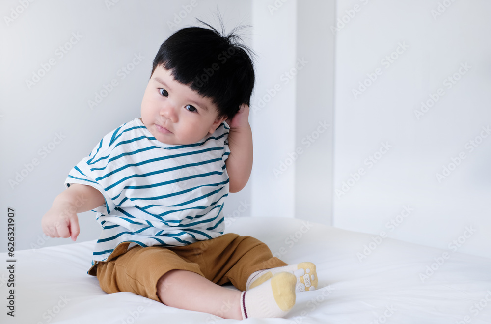 Close-up portrait of baby sitting and holding hair on the bed, asian baby happy and playing with copy space Close-up portrait of baby sitting and holding hair on the bed, asian baby happy and playing with copy space