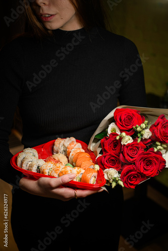 Young woman holding in hands large heart shaped sushi box with red roses bouquet