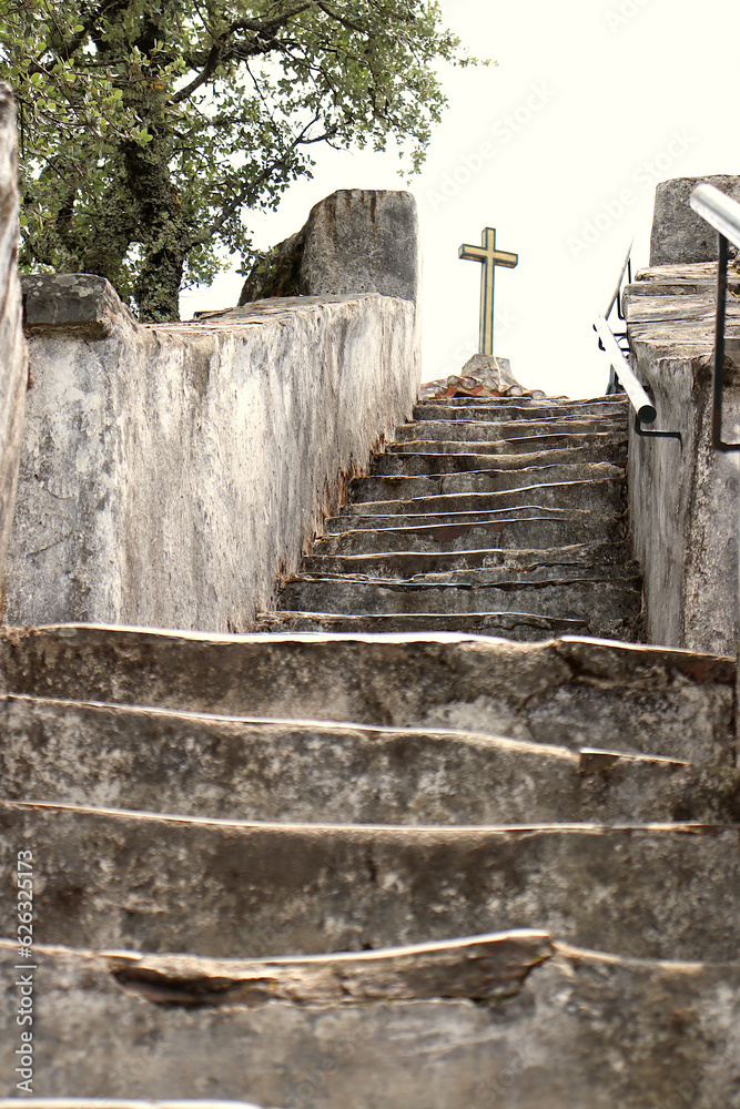 Christian stone cross on top of the church at Sanctuary of Nossa Senhora da Piedade, Lousã, Portugal. View from the bottom of the access stairs to the church.