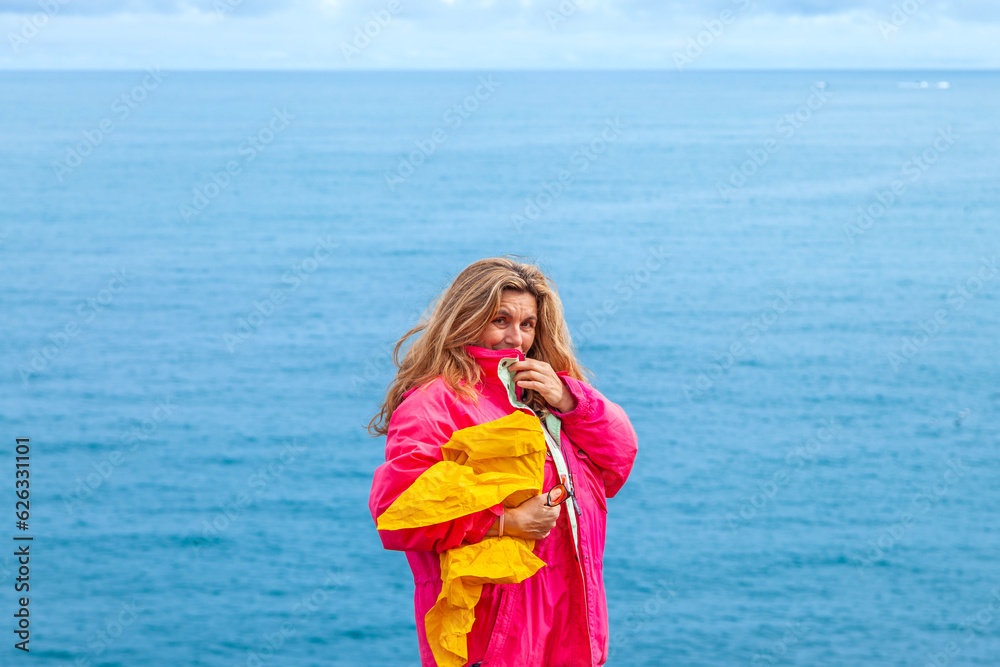 portrait of beautiful middle aged woman wearing a pink windbreaker in front of a blue sea portrait of beautiful middle aged woman wearing a pink windbreaker in front of a blue sea