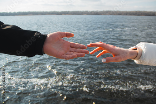 A guy and a girl in love, husband and wife, reach out to each other with their hands against the backdrop of the river and give each other love and support
