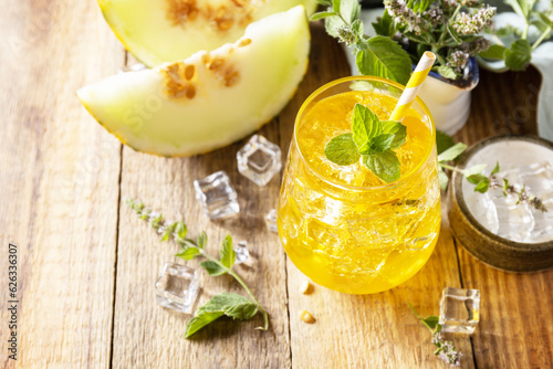 Melon lemonade in glasses with ice and mint on a wooden rustic table. Fresh refreshing fruity summer drink, seasonal beverages.