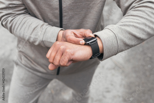 Unrecognizable man in sportswear standing and checking smart watch for time in daytime