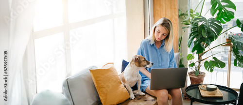 Working with dog. Woman in blue clothes using laptop sitting in cafe with her small white dog Jack Russell terrier. Remote work or study with pet friendly coworking space. Long horizontal banner 