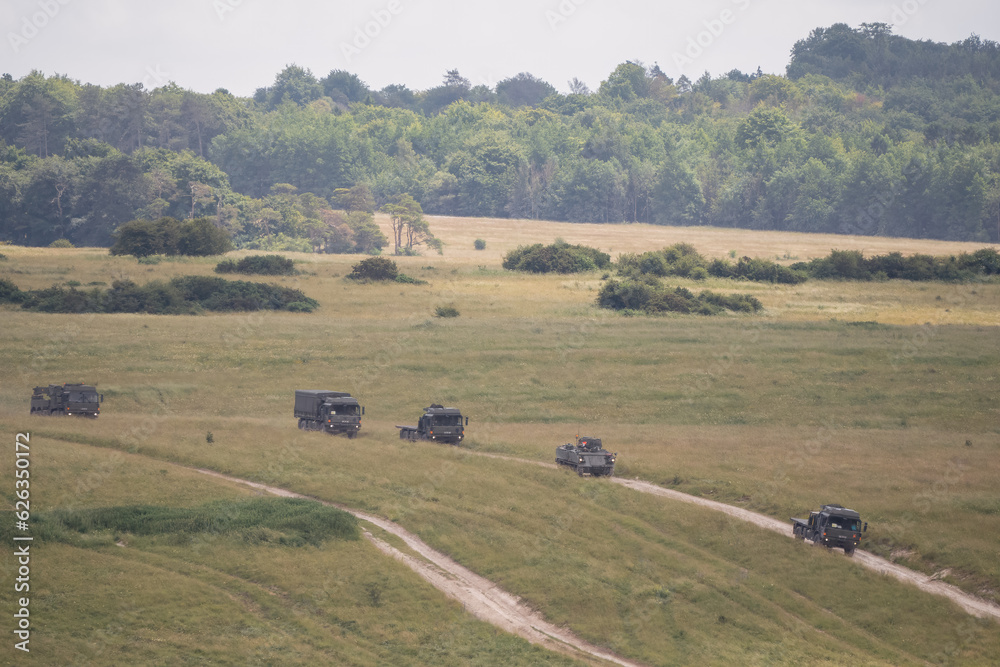 a convoy of British army vehicles moving across countryside on a military exercise