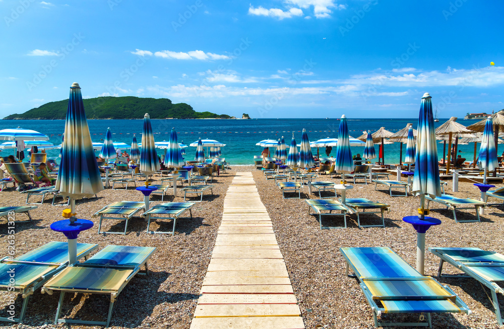 beautiful view of the sea beach, path to the sea, umbrellas and sun loungers, an island in the distance, Montenegro, the Adriatic Sea, tourism and summer travel